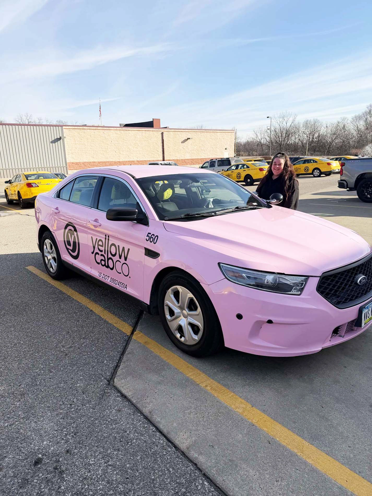 Professional photo of a pink taxi cab with the woman taxi driver standing next to it, the taxi has a black decal on the side that reads 